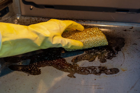 Hand in a rubber glove cleaning dirty oven with sponge and cleaner. Housework and housekeeping conceptの写真素材