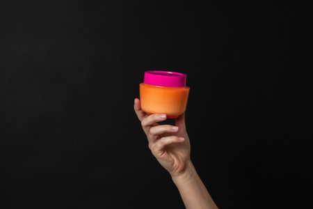 Cosmetic bottle for cream, mask or lotion on a hand with dark black background. Cosmetics productの写真素材