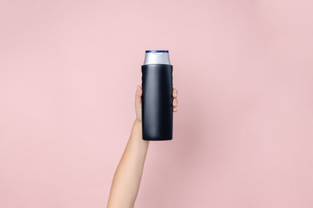Woman's hand holding shampoo bottle on the solid pink background. Cosmetics product package, your...