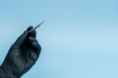 Cropped shot of professional dentist in black medical gloves with dental tool. Dental concept. Isolated on blue backgroundの写真素材