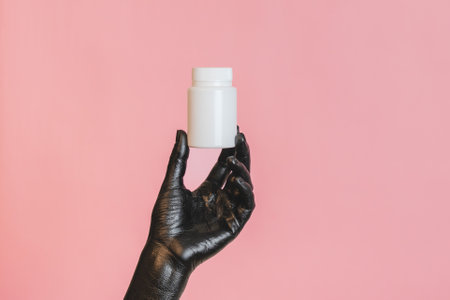 Black painted elegant woman's hand on her skin with a white cosmetic bottle. High Fashion art concept. Product cosmetic advertisingの写真素材