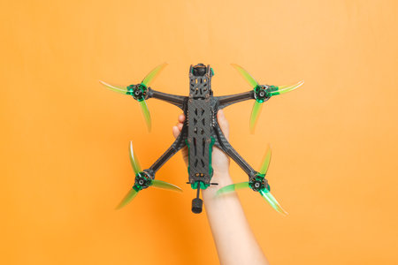 Hands holding a modern drone with camera on orange background