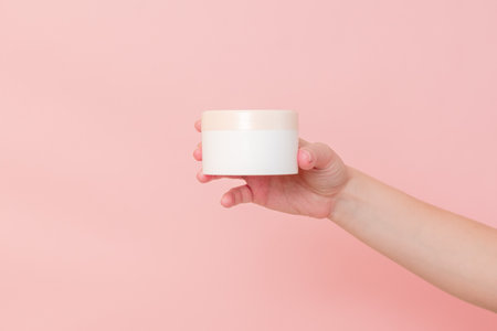 Hand holding jar of cosmetic cream on a pink background. Cosmetics beauty mockup for product brandingの写真素材