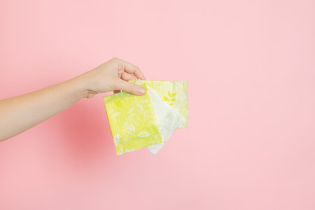 Packed sanitary napkins in a hand. Menstruation cycle, feminine hygiene and protection. Flat layout