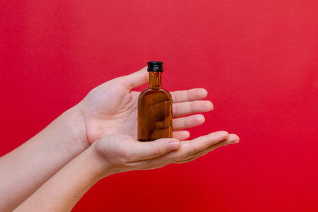 Elegant hand with small glass blank bottle mockup on the red background. Package for cosmetics product, nutritional supplements, mixture. Space for textの写真素材