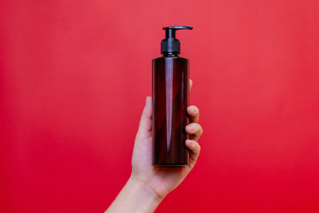 Elegant hand holding blank bottle mockup isolated on the solid red background. Package for cosmetics product, spa, beauty and luxury. Space for textの写真素材