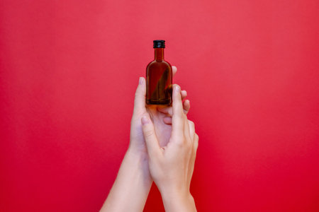 Hand with small glass blank bottle mockup on the red background. Package for cosmetics product, nutritional supplements, mixture, alcohol. Space for textの写真素材