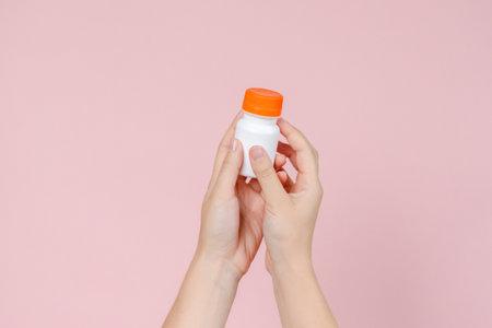 Elegant hand holding blank bottle mockup on the pink background. Package for cosmetics product, nutritional supplements, vitamins, spa, beauty and luxury. Space for textの写真素材