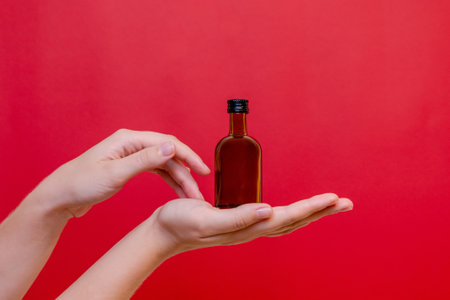 Elegant hand with small glass blank bottle mockup on the red background. Package for cosmetics product, nutritional supplements, mixture. Space for textの写真素材