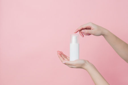 White unbranded cream bottle with pump in hand on pink background. Concept of beauty. Product...