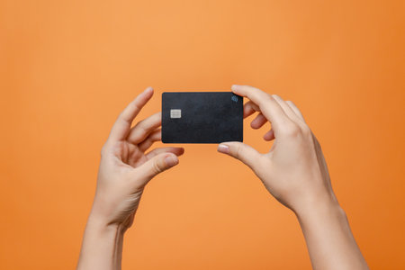 Close up elegant hand with a blank credit card with online service for mockup isolated on orange...