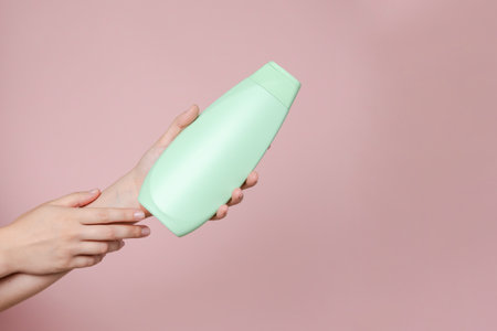 Elegant hand with shampoo light bottle isolated on the solid pink background. Package for cosmetics product, spa, beauty. Space for textの写真素材