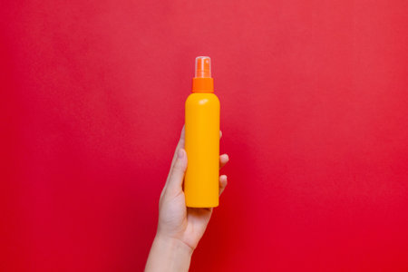 Female hand holding a orange spray cosmetic bottle on the solid red background.の写真素材