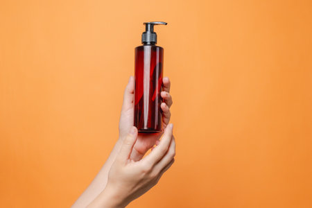 Elegant hand with blank bottle mockup isolated on the solid orange background. Package for cosmetics product, your brand, spa, beauty and luxury. Space for textの写真素材