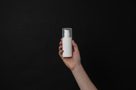 White cosmetic cream tube in hand on a black background. Presenting luxury skincare products.