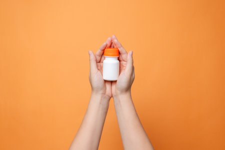 Blank bottle mockup in hand on the orange background. Package for cosmetics product, nutritional supplements, vitamins, spa, beauty and luxury. Space for textの写真素材