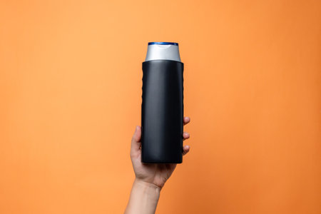 Shampoo bottle in female hand on the solid orange background. Cosmetics product package, spa. Space for textの写真素材