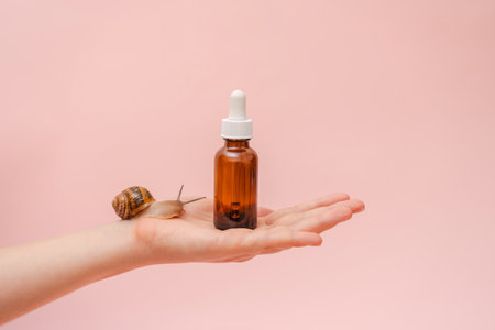 Cosmetic brown bottle with a snail in elegant hand. Concept of skin care product, spa, luxury, natural beautyの写真素材