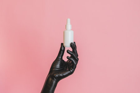 Black painted elegant woman's hand on her skin with a glass cosmetic bottle. Presenting luxury, fashion skincare productsの写真素材