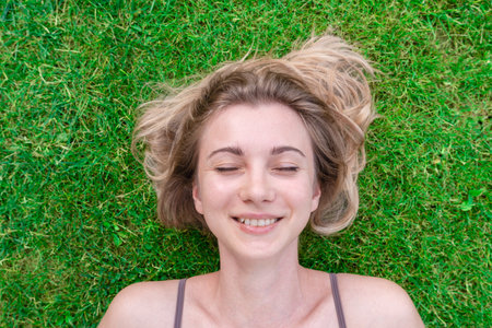 Close up of a beautiful young woman lying down in the green grassの写真素材
