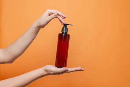 Elegant hand with blank bottle mockup isolated on the solid orange background. Package for cosmetics product, your brand, spa, beauty and luxury. Space for textの写真素材