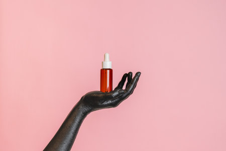 Black painted elegant woman's hand on her skin with a glass cosmetic bottle. Presenting luxury, fashion skincare productsの写真素材