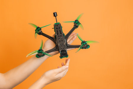 Hands holding a modern drone with camera on orange background