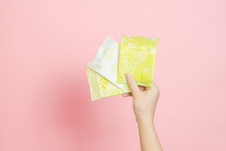 Packed sanitary napkins in a hand. Menstruation cycle, feminine hygiene and protection. Flat layoutの写真素材