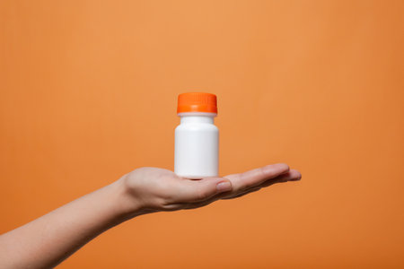 Blank bottle mockup in hand on the orange background. Package for cosmetics product, nutritional supplements, vitamins, spa, beauty and luxury. Space for textの写真素材