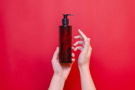 Elegant hand holding blank bottle mockup isolated on the solid red background. Package for cosmetics product, spa, beauty and luxury. Space for textの写真素材