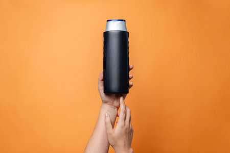 Shampoo bottle in female hand on the solid orange background. Cosmetics product package, spa. Space for textの写真素材