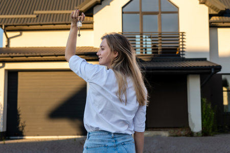Happy woman standing with house keys in front of a residential home. Real estate, moving home or renting property conceptの写真素材