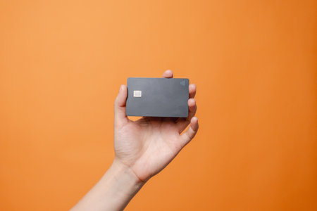 Close up elegant hand with a blank credit card with online service for mockup isolated on orange background. Modern way of banking and buyingの写真素材