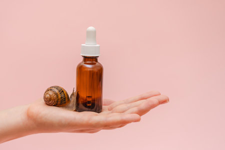 Brown bottle with a snail in elegant hand. Concept of skin care product, spa, luxury, natural beautyの写真素材