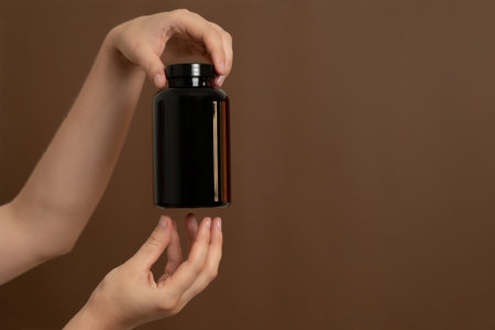 Human hands presenting a dark brown bottle against a brown background, ideal for health and beauty productsの写真素材
