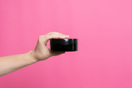 Hand holding a black cosmetic product jar, ideal for beauty and skincare concepts
