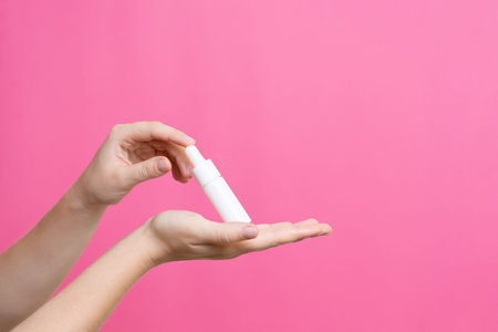 Hands holding a medical dropper bottle with a serum on a pink background