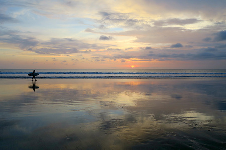 Lonely surfer silhouette walking along empty Kuta beach with sunset skyの写真素材