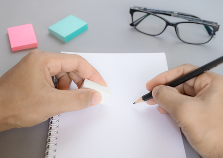 Close up view. Hands are holding a pencil and eraser on the white book.