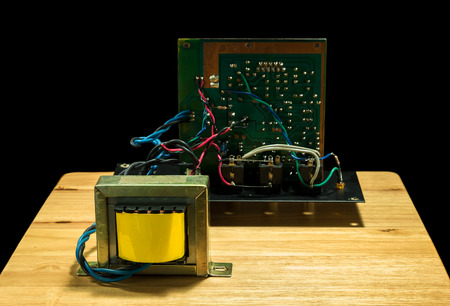 Old electric transformer with circuit bord and wire on wood plate and black background.