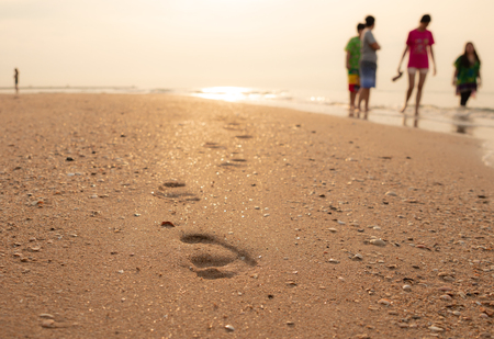 Close up view. Footprint of person walking on the sand. Shadow blur of people doing activities at the background. During the sunrise.のeditorial素材