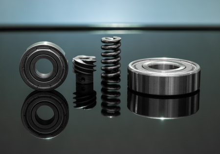 Close up view. Spare parts is spring with bearing and cog are small placed on black glass floor....