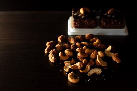 Close up view and copy space of light from the side. Almond and Cashew nuts on wooden table with cookie desserts in the shadows.の写真素材