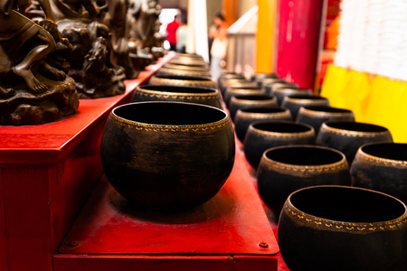 Close up view and low light. Many black bowls are placed on a wooden rack. For dropping coins. Which is how to make merit. In the temple of Thailand.の写真素材
