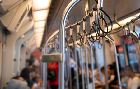 Low light and blurred view background. Empty handrail with many people in the sky train. Which is...