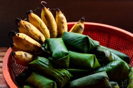 Low light view and close up. Ripe banana with Porridge rice wrapped in fresh banana leaves pile in basket. Is traditional dessert found in rural areas of Thailand.の写真素材