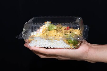 Close up view and black background. Fried egg with chicken green curry topped on rice. Carte boxed clear plastic packing. On a hands of people.の写真素材