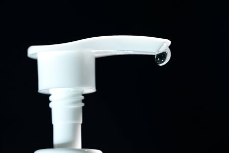Close up view and black background. Drop of alcohol gel hanging at tip of the dispenser from bottle.の写真素材
