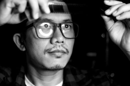 Black and white view and low light of blurry a man with wearing glasses. Then look the photographic film through the light.の写真素材