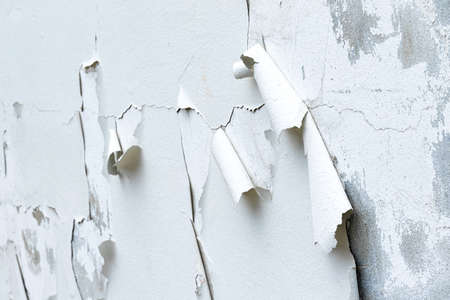 The old white concrete wall of building with cracks and sheet peeling of paint.